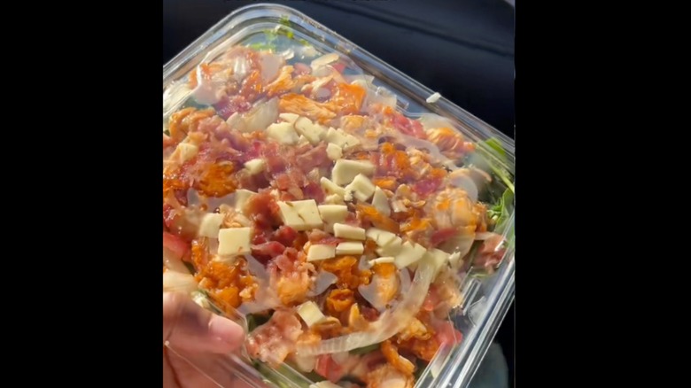 Hand holding a hot honey chicken tender salad in a plastic container