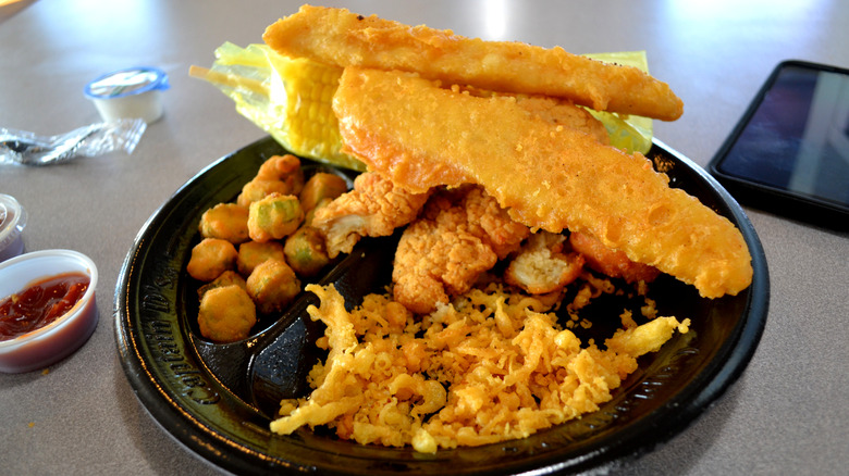 Captain D's meal of fried fish, corn on the cob, and fried okra on a black plate