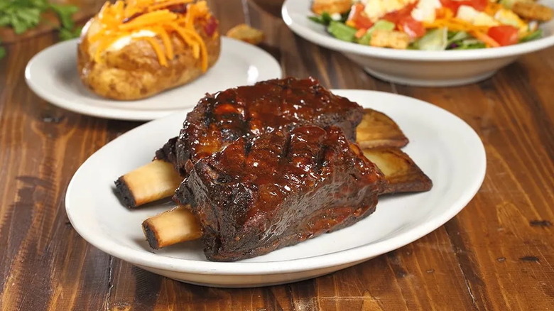 Ribs on a plate next to baked potato and salad.