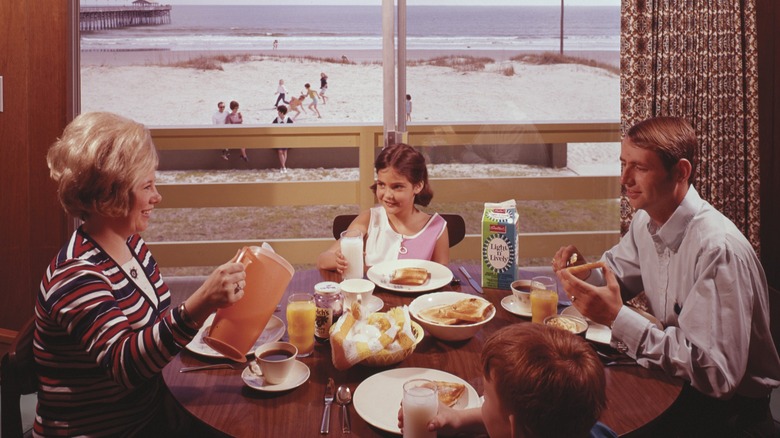 vintage image of a family in the 1960s eating breakfast together with a beach scene beyond the window