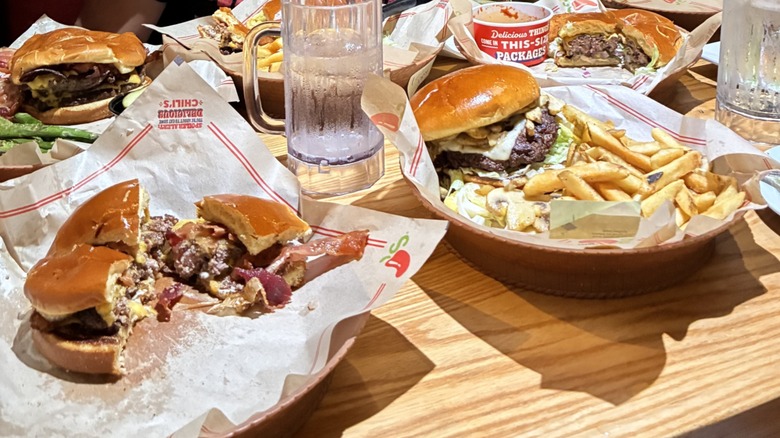 different burgers on a wooden table with large glasses of water