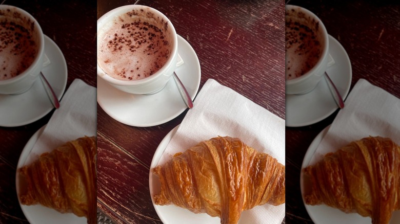 A cup of chocolat chaude alongside a croissant