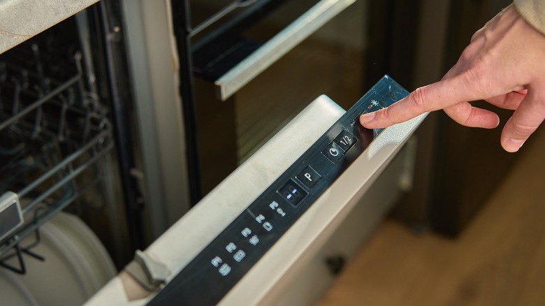 Close-up of female finger pressing button on dishwasher control panel.