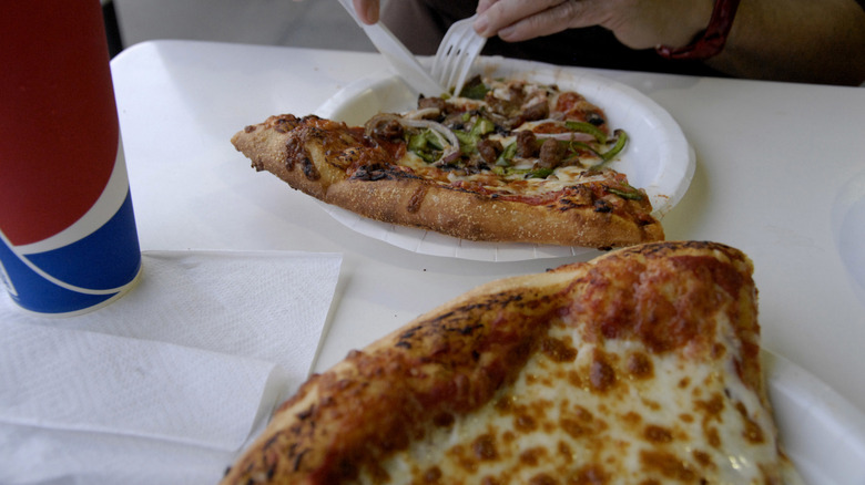 Person eating Costco combo pizza with plastic cutlery