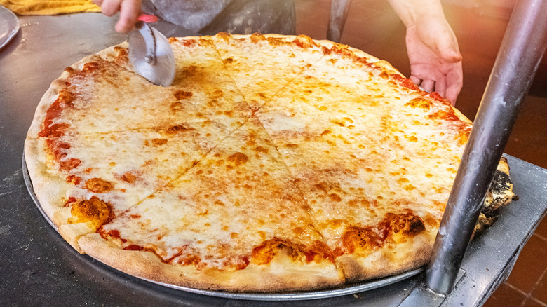 Person slicing an extra large cheese pizza