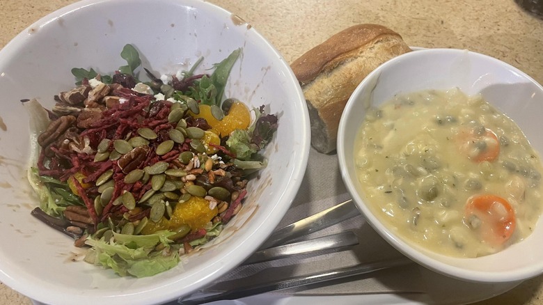 a tiny, messy salad and bowl of soup from Panera on a table, with a piece of bread behind them