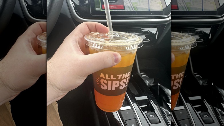 a hand holding a plastic cup filled with a beverage from Panera in a car