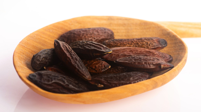 Tonka beans resting in a wooden bowl on a white surface