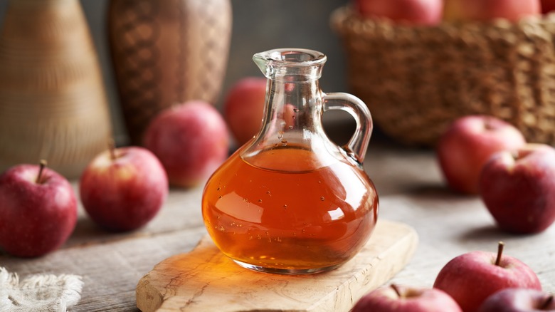 glass jug of apple cider with fresh apples in the background