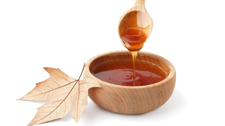 spoon dipping into a bowl of maple syrup next to a leaf