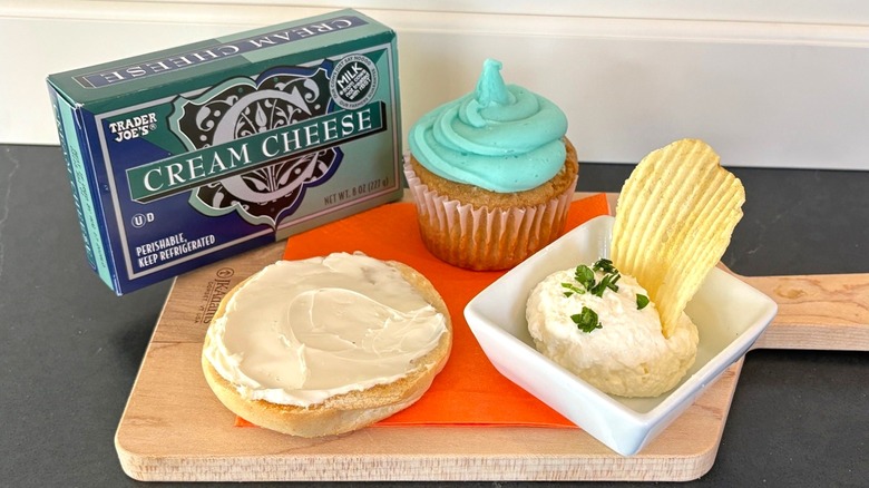 Trader Joe's cream cheese on a wooden cutting board with bagel, cupcake and chip dip