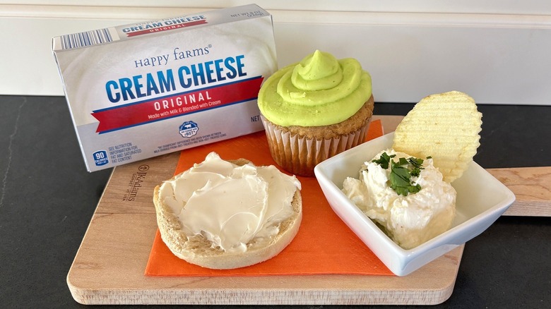 Aldi brand Happy Farms cream cheese on a wooden cutting board with bagel, cupcake and chip dip