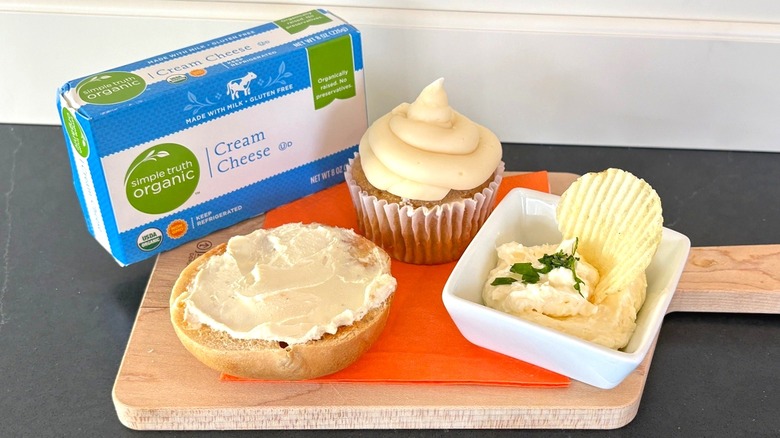 Simple Truth organic cream cheese on a wooden cutting board with bagel, cupcake and chip dip