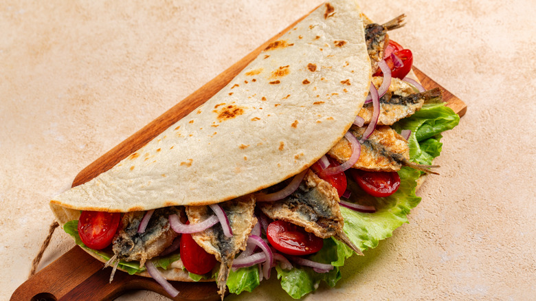 A closeup of a sardine taco on a serving board