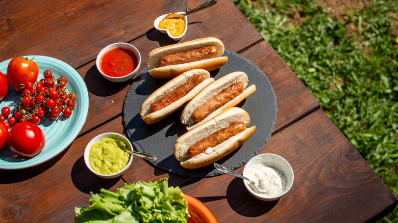Four hot dogs in buns sit on a plate on a wooden table.