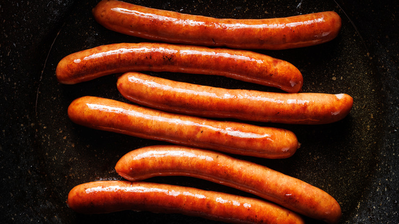 Six hot dogs cook in a frying pan.