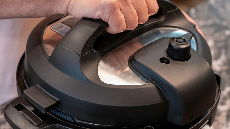 A hand grips the lid of an Instant Pot.