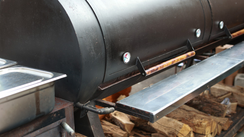 A smoker with a pile of wood underneath sits ready for use.