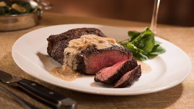 A dish containing Capital Grille's Bone-In Dry Aged NY Strips set against a golden tablecloth