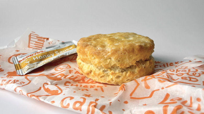 Popeye's biscuit on the fast food packaging next to a honey sauce packet