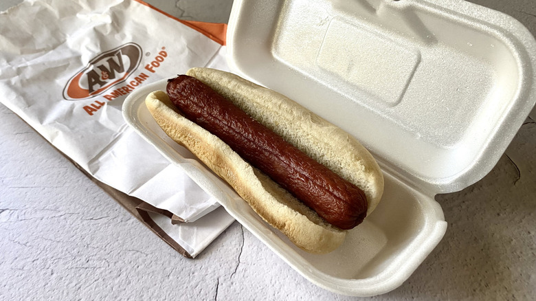 An A&W hot dog in a styrofoam container on top of a white paper bag