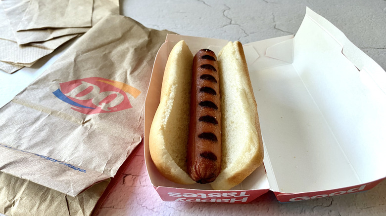 A Dairy Queen hot dog inside the take-out container next to a paper bag and napkins.
