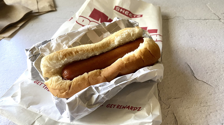 A Sheetz hot dog on top of the take-out packaging next to napkins