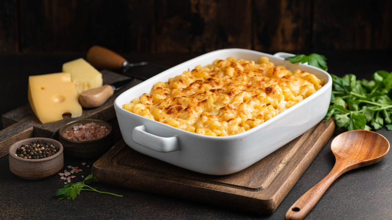 A casserole dish of mac and cheese on a wooden board