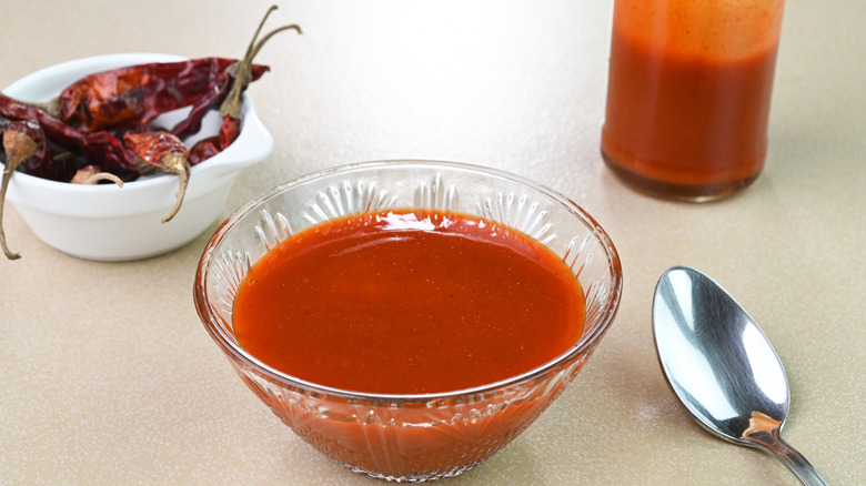 Smoky red chili sauce in a glass bowl with a dish of dried red chiles in the background