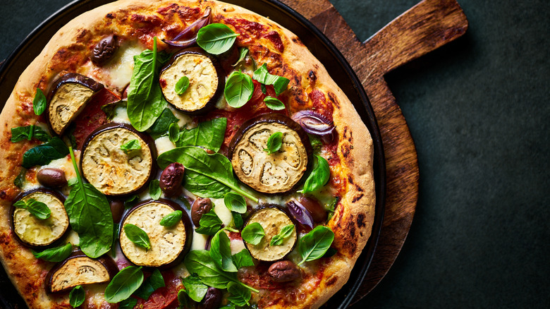 A vegetarian pizza topped with eggplant and spinach on a wooden tray