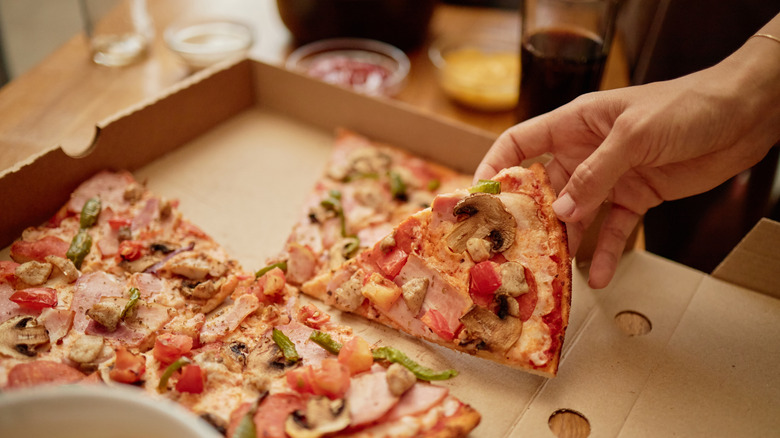 Person's hand is grabbing slice of pizza from a takeout box