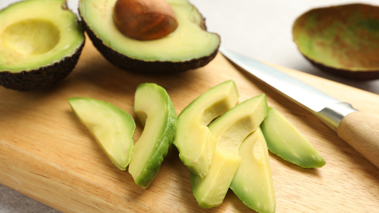 Sliced ripe avocado with halved avocado in the background