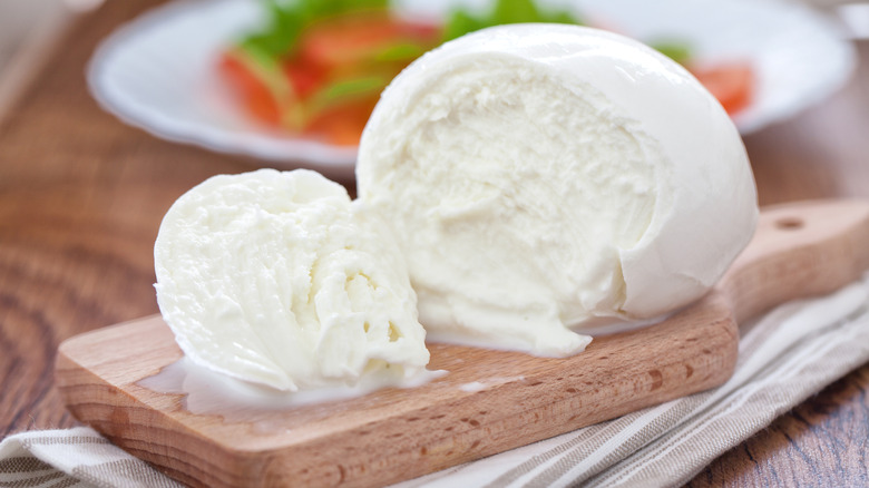 A halved ball of buffalo mozzarella on a wooden cutting board
