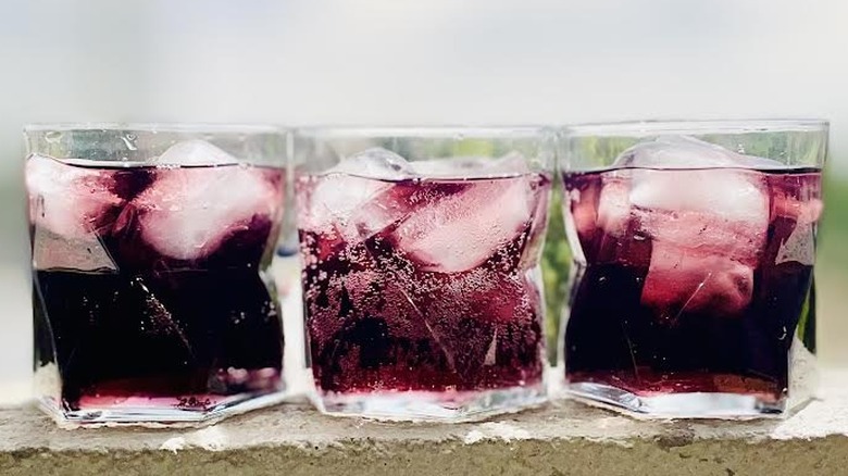 Three glasses filled with ice and grape soda sitting on a ledge