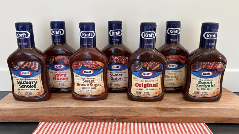 7 Kraft Barbecue Sauce bottles on cutting board next to red and white striped napkin
