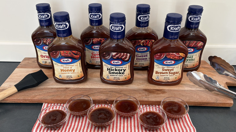7 Kraft BBQ sauce bottles on cutting board with sample dishes, bbq brush and tongs