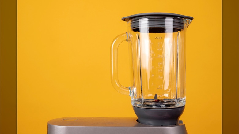 A blender with a orange wall in the background.
