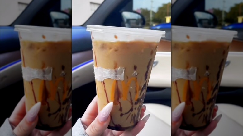 A hand holding up a clear plastic McDonald's coffee cup with a Snickers Iced Coffee.