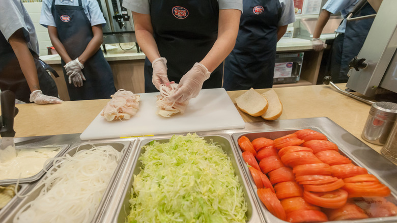 Jersey Mike's workers add onions, lettuce, and tomato to sub sandwiches