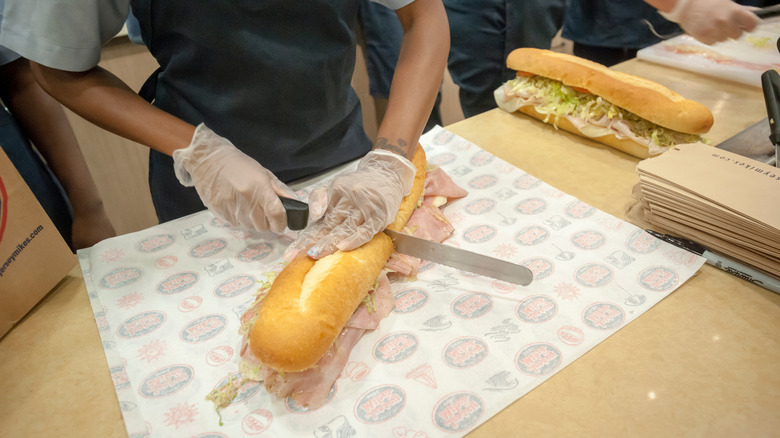 An employee cutting a Jersey Mike's sub with a knife