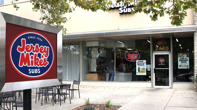 The entrance to a Jersey Mike's sub shop with chairs and tables outside