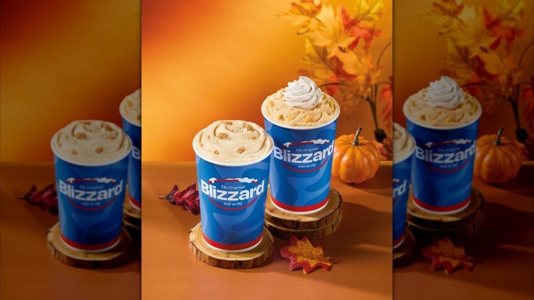 Two Caramel Apple Cheesecake Blizzard Treats in blue cups, one topped with whipped cream, on a table with fall decor.