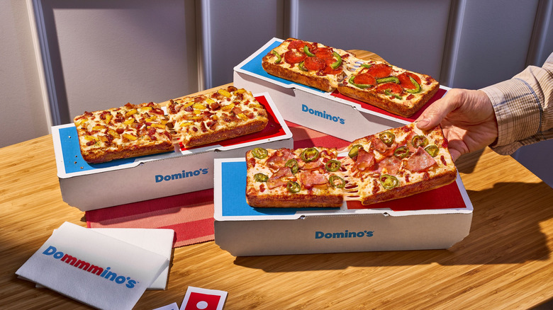 Three rectangular Detroit-style The Domino pizzas with a variety of toppings.