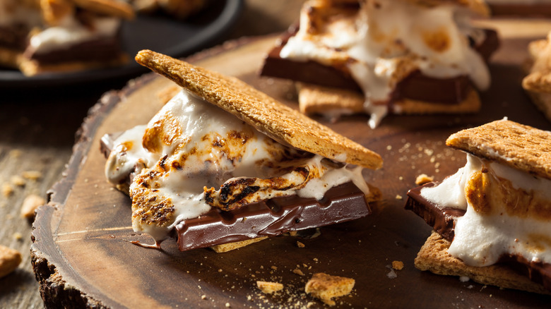 Several s'mores with toasted marshmallows sitting on a round section of a tree stump on a table.
