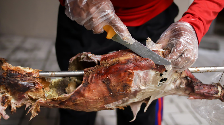 a man slicing barbecued goat off a spit roaster