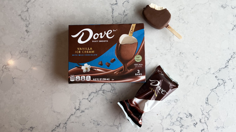 A DOVE Vanilla Ice Cream Bar Coated With Milk Chocolate with a bite taken out of it sits next to its package