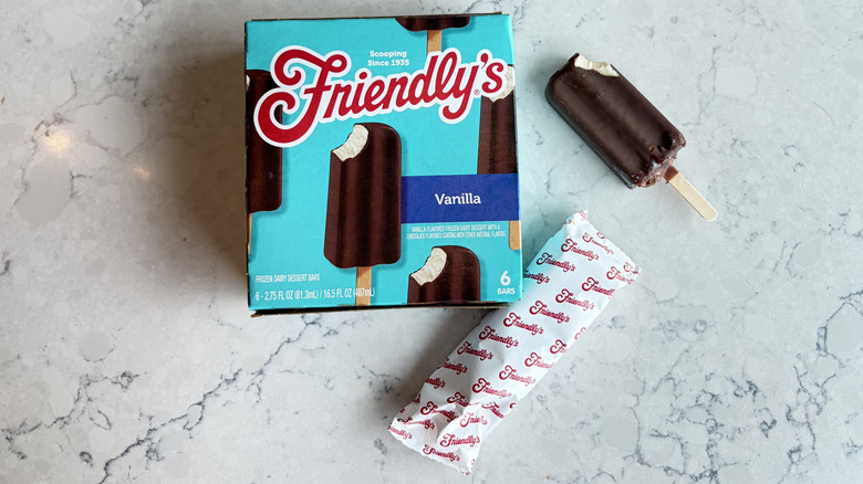 A Friendly's Vanilla Frozen Dairy Dessert Bar with a bite taken out of it sits next to its package