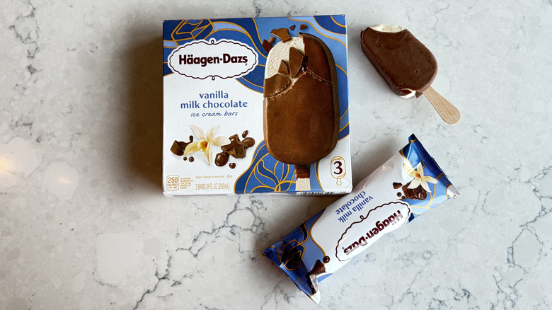 A Häagen-Dazs Vanilla Milk Chocolate Ice Cream Bar with a bite taken out of it sits next to its package