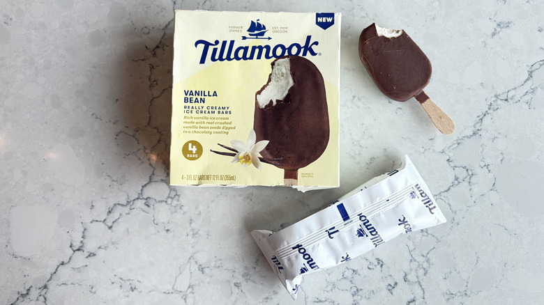 A Tillamook Vanilla Bean Really Creamy Ice Cream Bar with a bite taken out of it sits next to its package