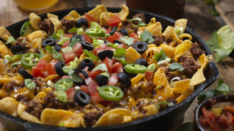 Round casserole with Frito pie, with Fritos, sliced black olives, tomatoes, ground beef, cheese, and sliced jalapenos